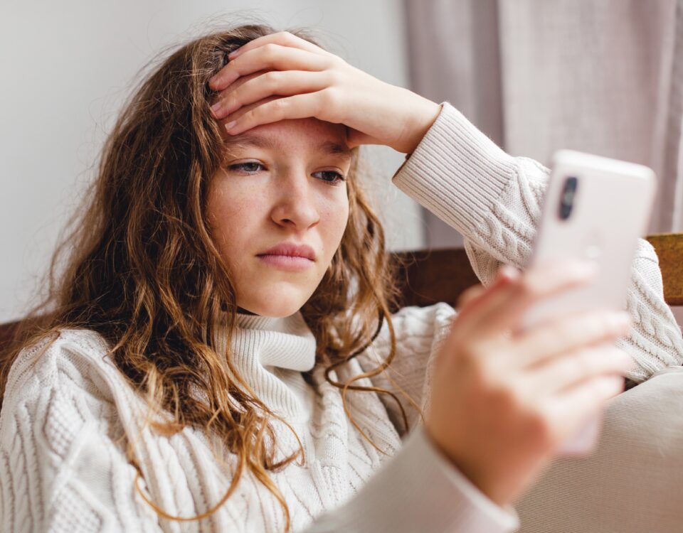 Adolescente inquiète regardant son smartphone, symbolisant le harcèlement scolaire et le cyberharcèlement sur les réseaux sociaux.